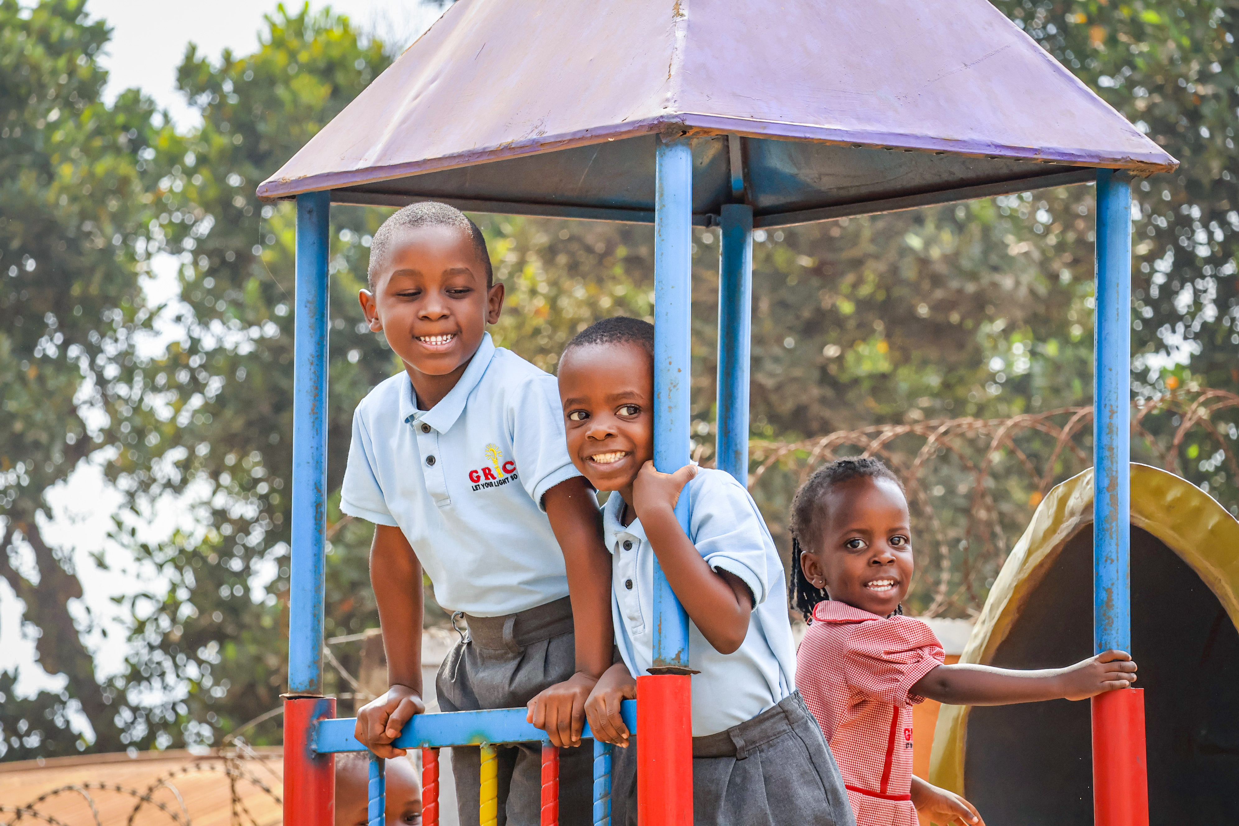 Three GRICS learners posing together under the playground shelter